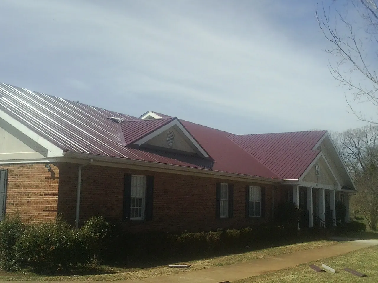 Red metal roof with gabled entries on a long brick building, from a Hail Damage Roof Repair job in Maybee