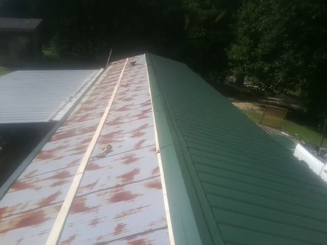 Old rusted panels beside newly installed green metal roofing — Wind Damage Roof Repair by Roofing Brothers in Maybee