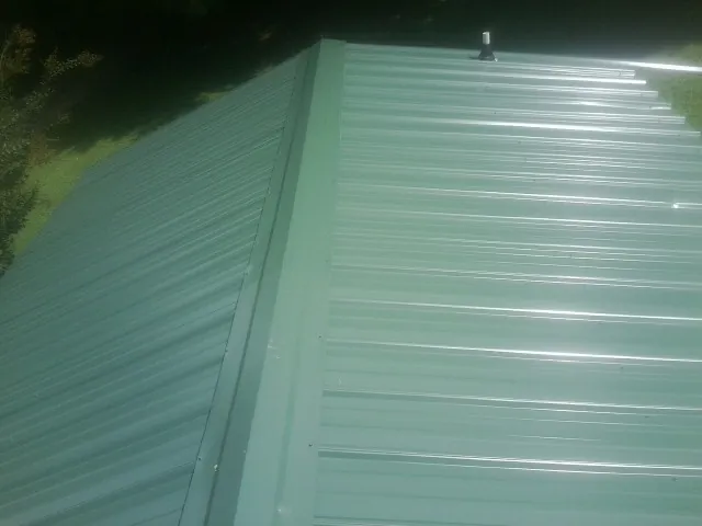 New green metal panels meeting at the ridge of a roof — Flat Roof Repair work by our crew in Maybee
