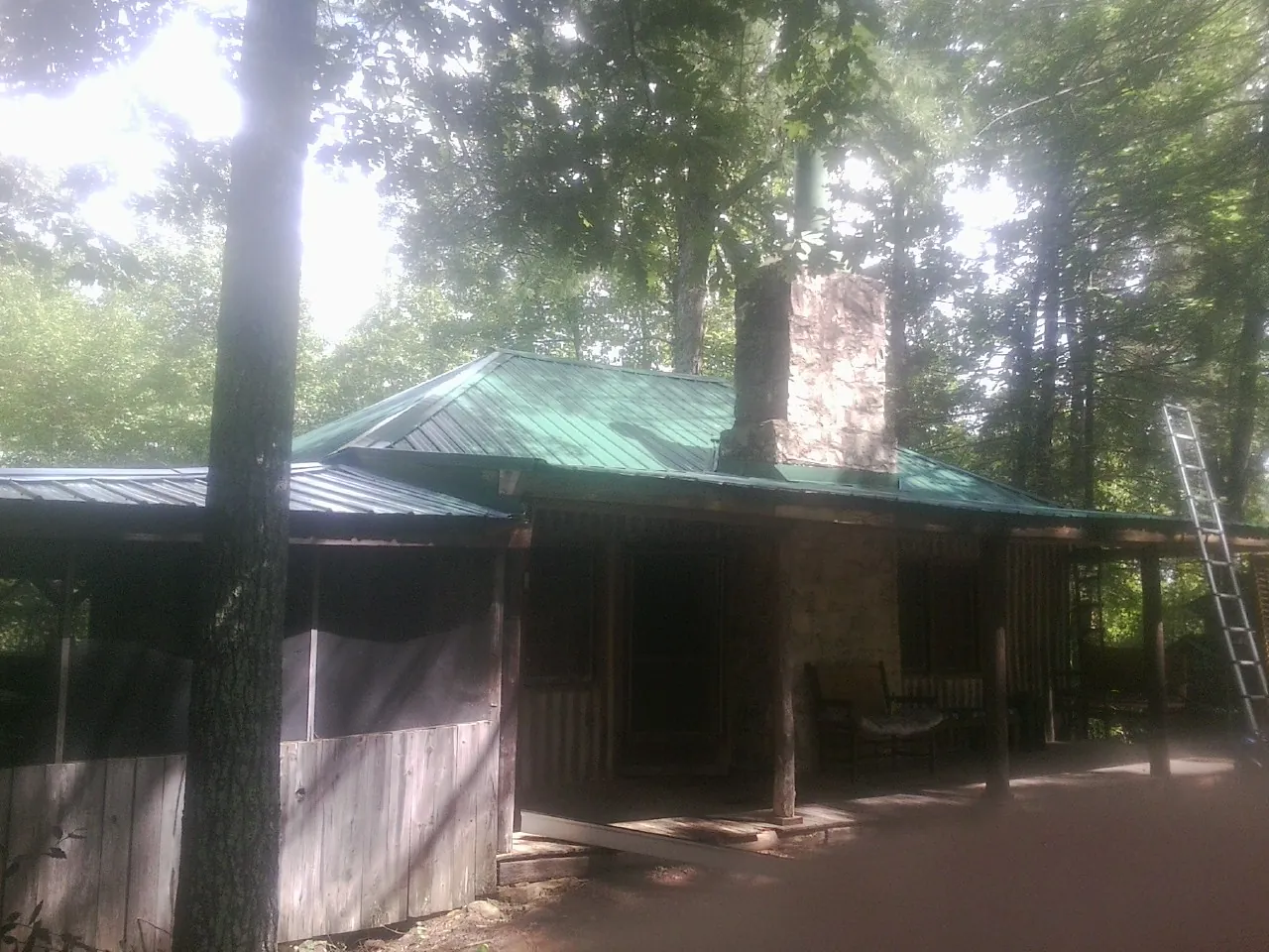 Green metal roof and stone chimney above a log cabin porch in Maybee