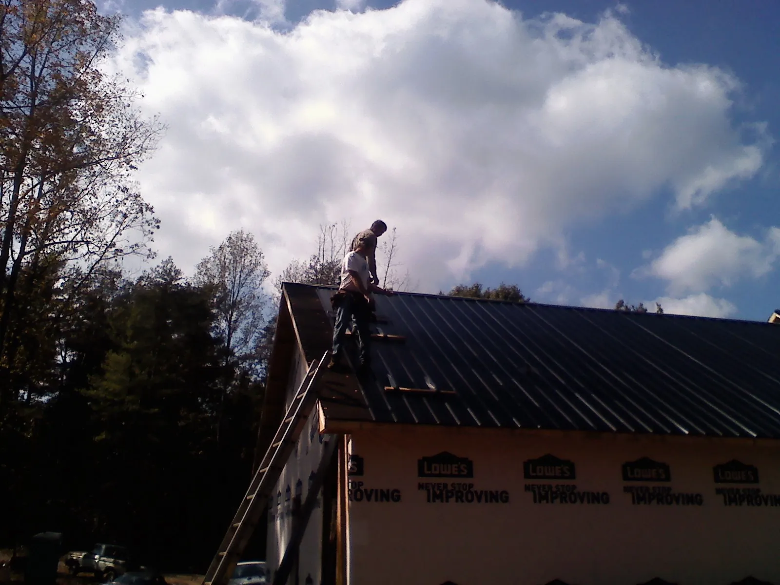 Roofer fastening dark metal panels high against a cloudy sky, from a Roof Inspection job in Maybee